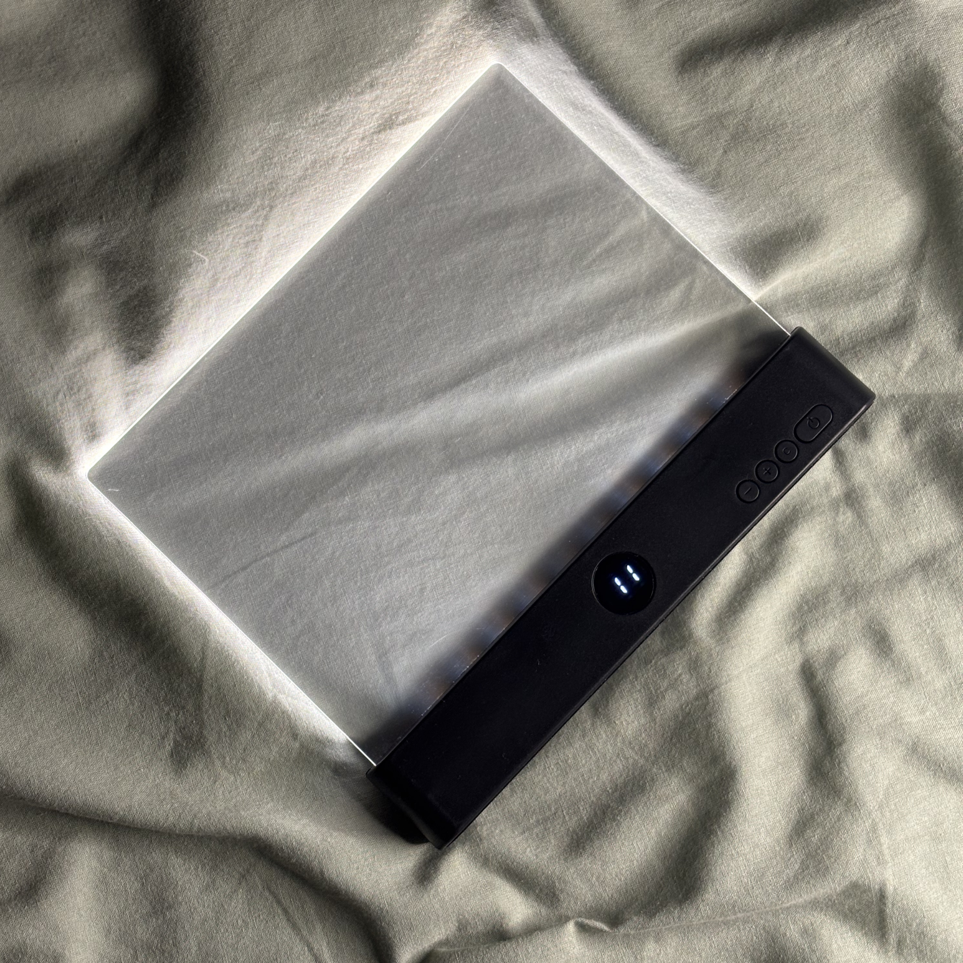 NachtLeser Klemmleselampe in Schwarz auf grauer Bettwäsche, flacher Lichtdiffusor mit klarem Acrylpanel